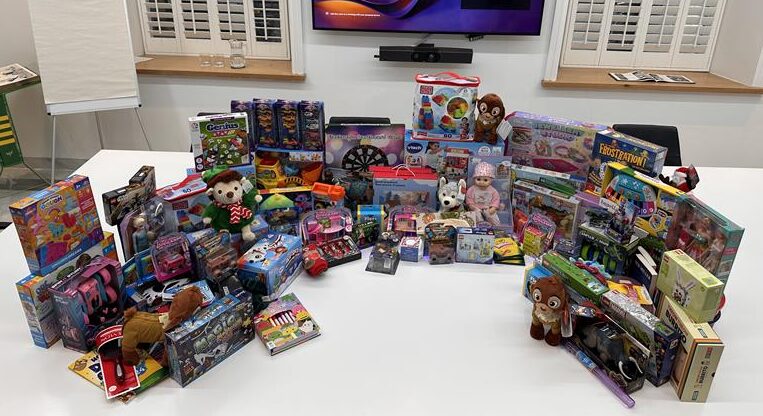 Collection of gifts donated through the Mission Christmas gift drive displayed on the board table of the Ramsbottom office
